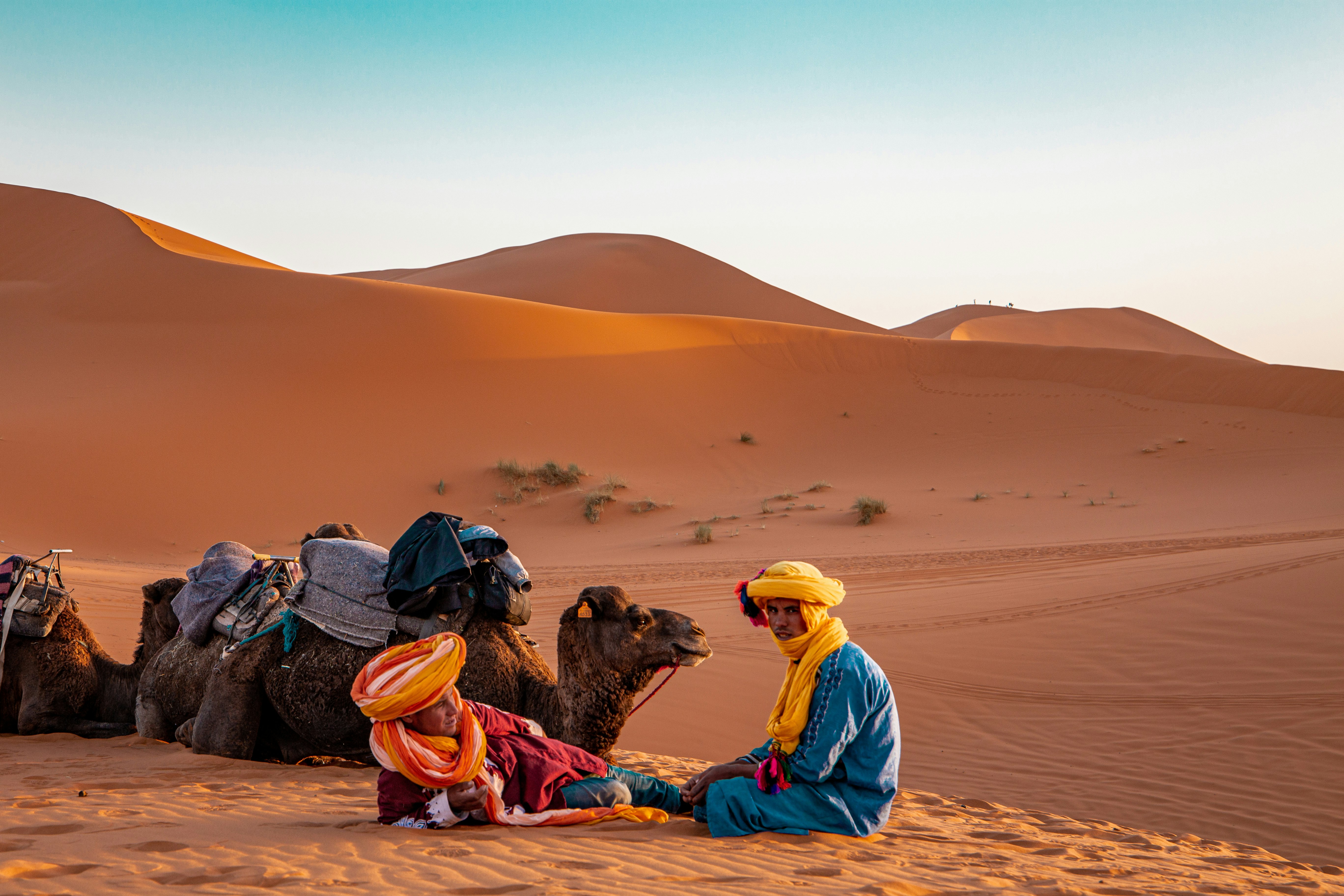 man in yellow robe sitting on brown sand during daytime